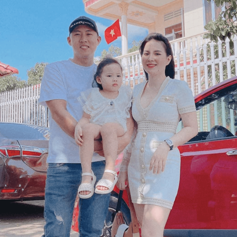Gia đình ba người chụp ảnh trước nhà bên xe hơi đỏ
